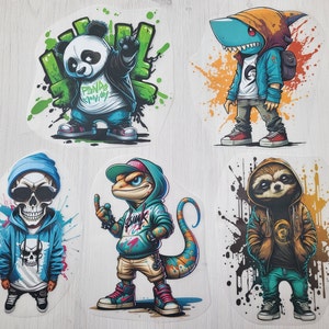 Könnte beinhalten: Eine Sammlung von fünf Cartoon-Aufklebern mit anthropomorphen Charakteren. Die Aufkleber zeigen einen Panda, einen Hai, einen Totenkopf, eine Eidechse und ein Faultier, alle in Streetwear gekleidet. Jeder Charakter ist vor einem farbenfrohen Spritzerhintergrund platziert.