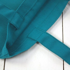 May include: Close-up of a teal blue tote bag with fabric handles. The bag is made of a thick, durable canvas material.
