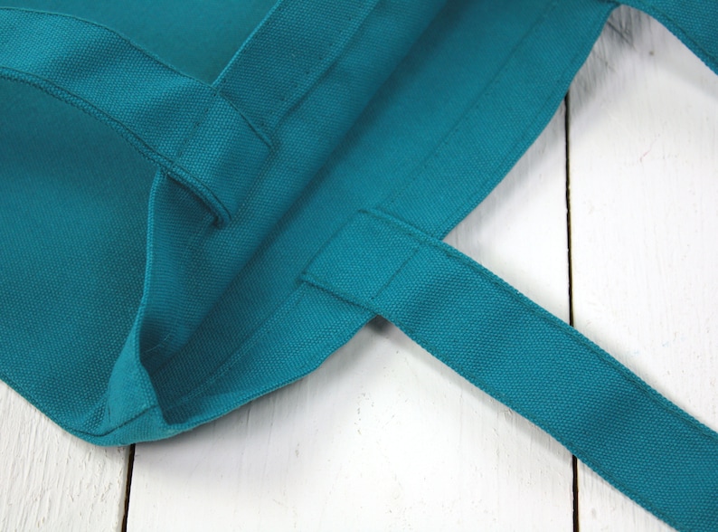 May include: Close-up of a teal blue tote bag with fabric handles. The bag is made of a thick, durable canvas material.