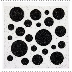 Op de afbeelding: Een vel wit papier met zwarte glitter stippen in verschillende maten. De stippen zijn in een willekeurig patroon gerangschikt.