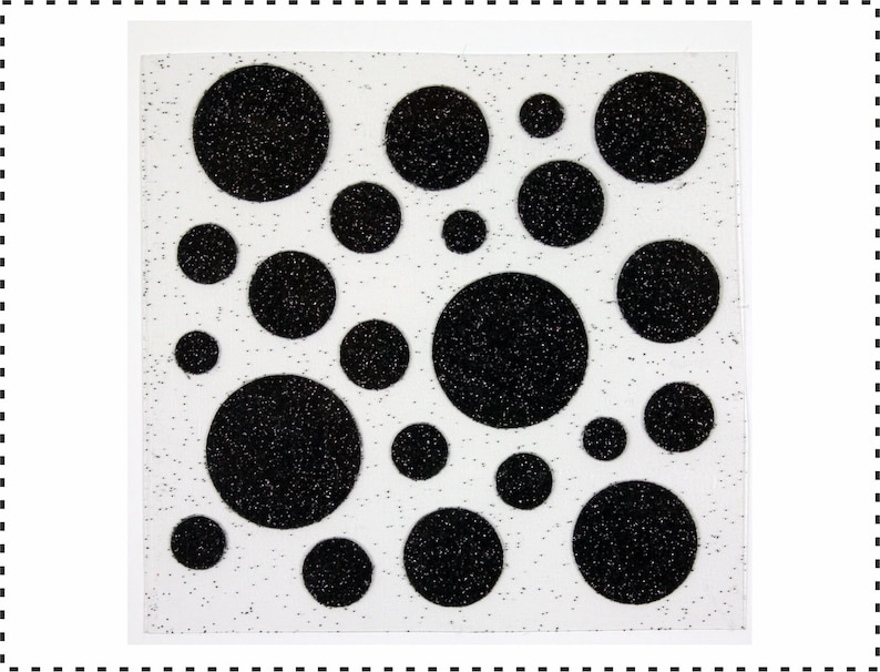 Op de afbeelding: Een vel wit papier met zwarte glitter stippen in verschillende maten. De stippen zijn in een willekeurig patroon gerangschikt.