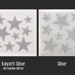 Op de afbeelding: Twee vellen met zilveren glitterster stickers. Het linker vel heeft sterren met iriserende glitter. Het rechter vel heeft sterren met effen zilveren glitter. De tekst "Konfetti Silber mit buntem Glitzer" staat onder het linker vel en de tekst "Silber" staat onder het rechter vel.