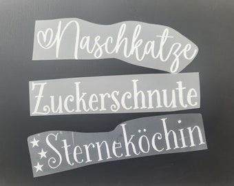 Op de afbeelding: Drie witte vinyl stickers met Duitse woorden op een zwarte achtergrond. De bovenste sticker zegt "Naschkatze", de middelste sticker zegt "Zuckerschnute" en de onderste sticker zegt "Sterneköchin".