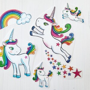 Könnte beinhalten: Eine Sammlung farbenfroher Einhorn-Aufkleber. Die Aufkleber zeigen weiße Einhörner mit Regenbogenmähnen und -schwänzen, einen Regenbogen und eine Sternenspur. Die Einhörner haben rosa, blaue und grüne Akzente.