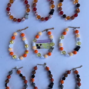 May include: Nine colorful beaded dog collars with a pug charm. The collars are in various colors, including orange, yellow, red, white, and black. The collars are decorated with different patterns, including flowers, pumpkins, and candy corn. The collars are all made with large, chunky beads.