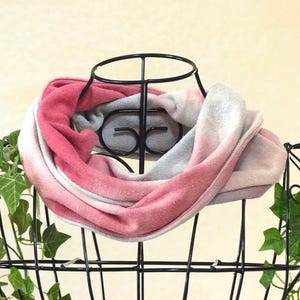 Könnte beinhalten: Ein weicher, rosa, weiß und grau farbverlaufender Loop-Schal. Der Schal wird auf einem schwarzen Metallständer mit rundem Oberteil präsentiert. Der Farbverlauf geht von einem tiefen Rosa zu einem hellen Grau über.