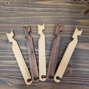 May include: Five wooden bottle openers in varying shades of brown and tan are arranged on a dark wood surface. Each opener has a unique cat-shaped design at the top and a circular opening at the bottom for leverage.