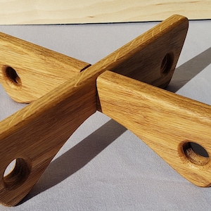 May include: A wooden trivet with a cross-shaped design. The trivet is made of light brown wood and features four curved arms, each with a circular hole. The arms are joined in the center, creating a stable base for hot dishes.