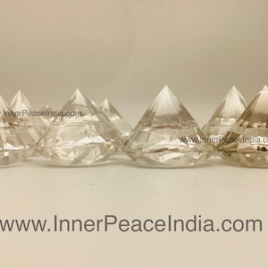 Puede incluir: Varios objetos transparentes en forma de diamante de cristal facetado están dispuestos en fila. Los cristales son transparentes y reflejan la luz, creando un efecto brillante. La dirección del sitio web www.InnerPeaceIndia.com se muestra abajo.