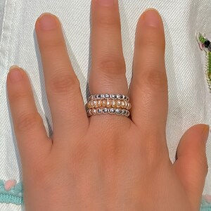 May include: A set of three beaded rings, one silver and two with a light peach colour.