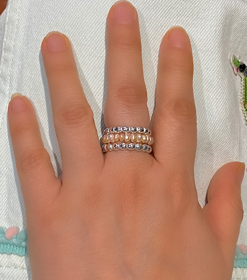 May include: A set of three beaded rings, one silver and two with a light peach colour.