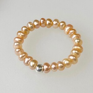 May include: A delicate ring made of a strand of small, pale pink pearls with a single silver bead accent.