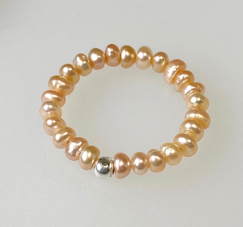 May include: A delicate ring made of a strand of small, pale pink pearls with a single silver bead accent.