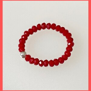 May include: A red beaded ring with a silver bead accent. The ring is made of small, faceted beads.