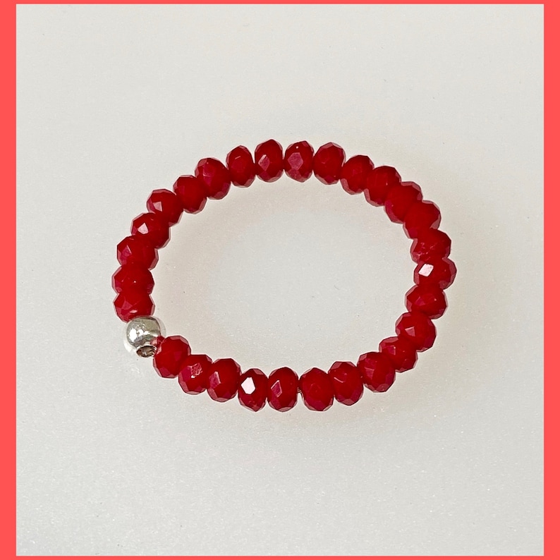 May include: A red beaded ring with a silver bead accent. The ring is made of small, faceted beads.