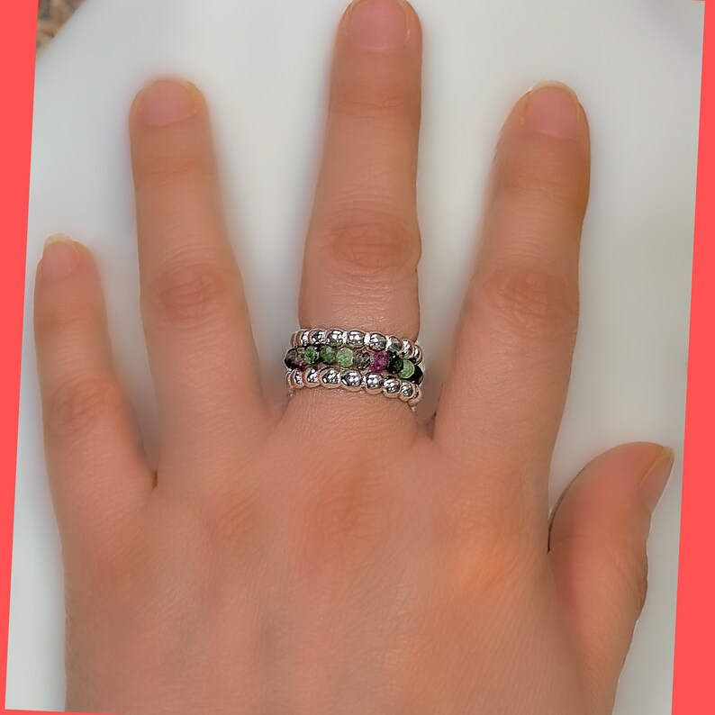 May include: A silver ring with three bands of small, colourful beads. The beads are green, pink, and black.