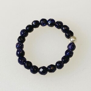 May include: A dark blue beaded ring with a silver bead accent. The beads are faceted and have a sparkly finish.