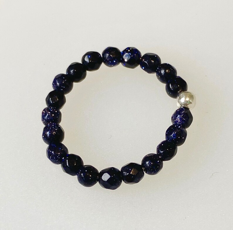 May include: A dark blue beaded ring with a silver bead accent. The beads are faceted and have a sparkly finish.