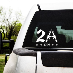 May include: White vinyl sticker with the text "2A" and two stylized rifles crossed over the letter "A". The text "1776" is below the rifles. There are four stars around the text.