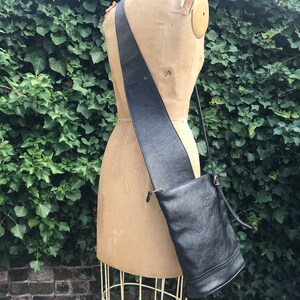 May include: A black leather shoulder bag with a long strap. The bag has a bucket shape and a zipper closure.