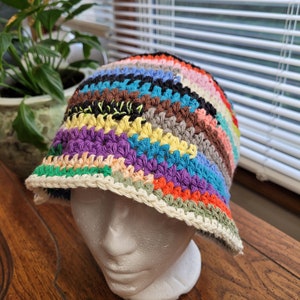 May include: A colorful crocheted bucket hat with a wide brim. The hat is made with a variety of colors, including red, orange, yellow, green, blue, purple, and brown.