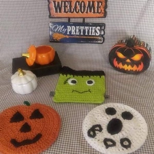 May include: A collection of Halloween themed crocheted items including a pumpkin, ghost, and Frankenstein. The crocheted items are displayed on a checkered tablecloth with a sign that reads "Welcome My Pretties".