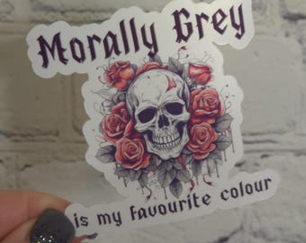 May include: A white sticker featuring a black and white skull surrounded by red roses. The text "Morally Grey is my favourite colour" is printed on the sticker.