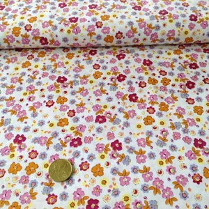 Könnte beinhalten: Weißer Stoff mit einem kleinen Blumendruck in den Farben Rosa, Orange, Gelb und Lila. Der Stoff ist in der Mitte gefaltet und eine Münze liegt darauf.