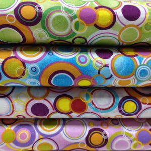 Könnte beinhalten: Vier Stoffmuster mit einem bunten, sich wiederholenden Muster aus Kreisen und Ringen. Die Farben umfassen Grün, Blau, Weiß, Lila, Orange, Gelb und Rot.