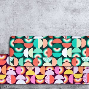 Könnte beinhalten: Drei Rollen buntes Geschenkpapier mit einem geometrischen Muster aus Kreisen und Halbkreisen. Das Papier ist grün, rosa und gelb mit weißen Akzenten.