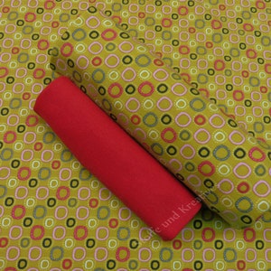 Può includere: Un rotolo di tessuto rosso con un rotolo di tessuto giallo con un motivo di cerchi rosa, rossi e grigi in cima. Il tessuto è stampato con il testo "Cafe und Kreativ".
