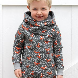 K&ouml;nnte beinhalten: Ein kleines Kind tr&auml;gt einen grauen Kapuzenpullover mit einem Fuchs-Druck. Der Pullover hat eine gro&szlig;e Kapuze und eine K&auml;ngurutasche. Das Kind l&auml;chelt und schaut in die Kamera.