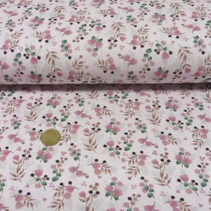 Könnte beinhalten: Weißer Stoff mit einem sich wiederholenden Muster aus rosa Blüten, grünen Blättern und braunen Stielen. Der Stoff ist gerollt und zeigt das Muster im Detail. Eine Münze liegt auf dem Stoff.