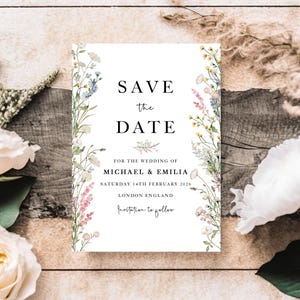 Könnte beinhalten: Eine weiße Hochzeitskarte mit floralen Verzierungen und dem Text "SAVE the DATE". Die Einladung enthält die Details für die Hochzeit von Michael & Emilia, die am 14. Februar 2026 in London, England, stattfindet.