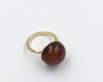 May include: A gold ring with a large, round, brown amber stone.