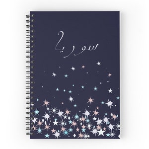 Può includere: Un quaderno a spirale blu scuro con il testo "سوره" in scrittura bianca. La copertina è decorata con una dispersione di stelle bianche, blu e rosa.