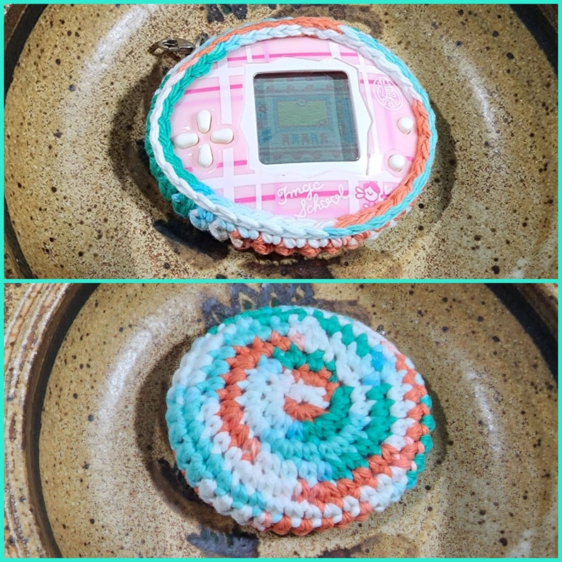 May include: A pink and white digital pet toy with a screen that says "Tamagotchi" and "Magic School" is wrapped in a crocheted cover with white, blue, and orange yarn. The toy is sitting in a brown ceramic bowl.