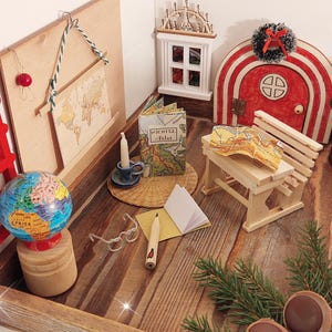 Könnte beinhalten: Ein Miniatur-Holzspielset mit einer roten Leiter, einem Globus, einer kleinen Holzbank, einem Buch, einer Kerze, einem Notizbuch, einem Bleistift und einer kleinen Holztür mit roten und weißen Streifen. Das Spielset befindet sich auf einer Holzoberfläche mit einem grünen Kiefernzweig.