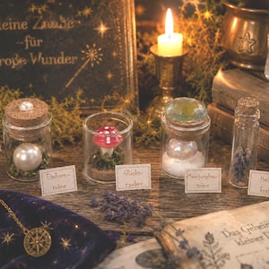Könnte beinhalten: Vier kleine Glasfläschchen mit Korken, gefüllt mit einer weißen Perle, einem roten Fliegenpilz, einer irisierenden Kugel und getrocknetem Lavendel. Jedes Glas hat ein kleines Papieretikett mit der Aufschrift Einhornträne, Glückszauber, Meerjungfrauträne, Heilkraft.