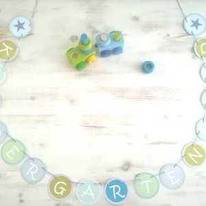 Könnte beinhalten: Ein blauer und grüner Spielzeugzug mit einem Banner, auf dem in weißen Buchstaben "Kindergarten" auf weißem Hintergrund steht.