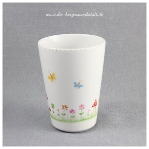 Puede incluir: Taza de cer&aacute;mica blanca con un dise&ntilde;o caprichoso que presenta mariposas, flores y setas. La taza tiene un borde dorado y una l&iacute;nea punteada alrededor de la parte superior.