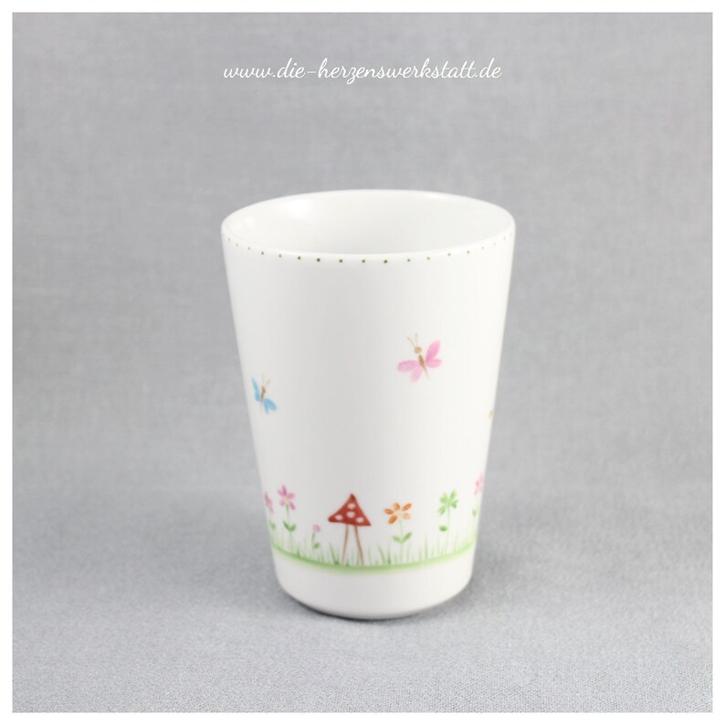 Puede incluir: Taza de cer&aacute;mica blanca con un borde dorado y un dise&ntilde;o caprichoso de mariposas, flores y un hongo. La taza est&aacute; decorada con un estilo delicado pintado a mano.