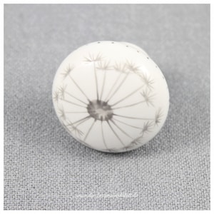 Puede incluir: Pomo de cerámica blanco con un diseño de diente de león gris.