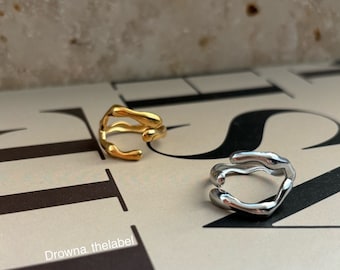 May include: Two abstract shaped rings, one gold and one silver. The rings are made of metal and have a unique, organic design.