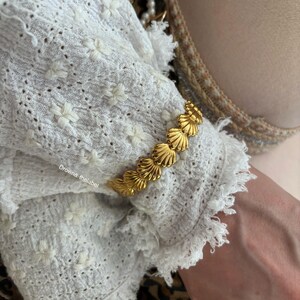 Könnte beinhalten: Goldarmband mit Muschel-Design. Das Armband besteht aus mehreren verbundenen Muscheln.