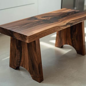 May include: A handcrafted wooden bench with a rich, dark brown finish. The bench features a rectangular top and four sturdy legs. The wood grain is visible, adding to its natural aesthetic. This piece is suitable for indoor use.