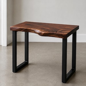 May include: A rectangular table featuring a dark brown wood slab top with a natural live edge along the front side. The table is supported by two black metal U-shaped legs that provide a stable base for the thick, polished wooden surface.