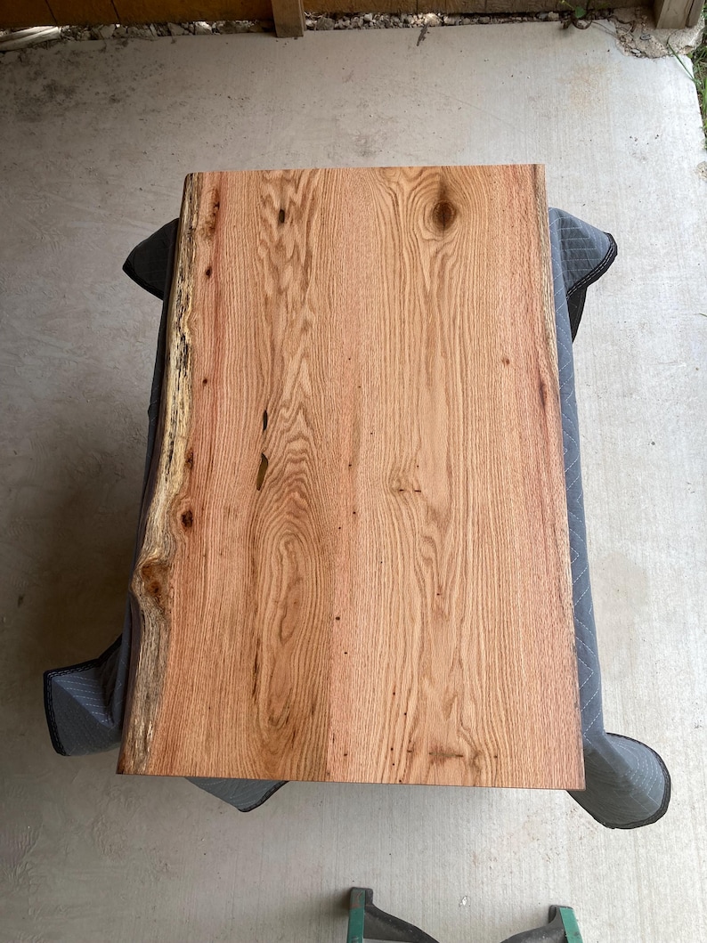 May include: A large, rectangular piece of wood with a live edge. The wood has a natural, light brown color with a grain pattern. The wood is smooth and polished.
