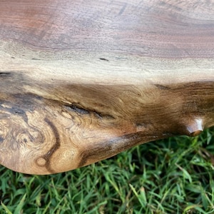 May include: Close-up of a dark brown wooden table top with a natural edge. The wood grain is visible and has a rich, dark brown color. The table top is smooth and polished.