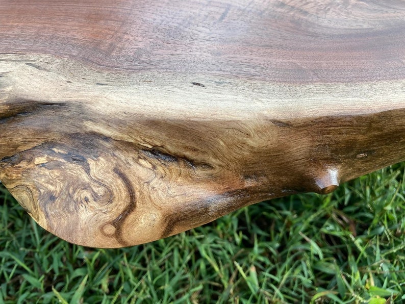 May include: Close-up of a dark brown wooden table top with a natural edge. The wood grain is visible and has a rich, dark brown color. The table top is smooth and polished.